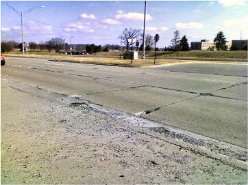 This picture shows a severely distressed concrete pavement, with severe spalling along the transverse and longitudinal joints. Debris can be seen along the side of the pavement.